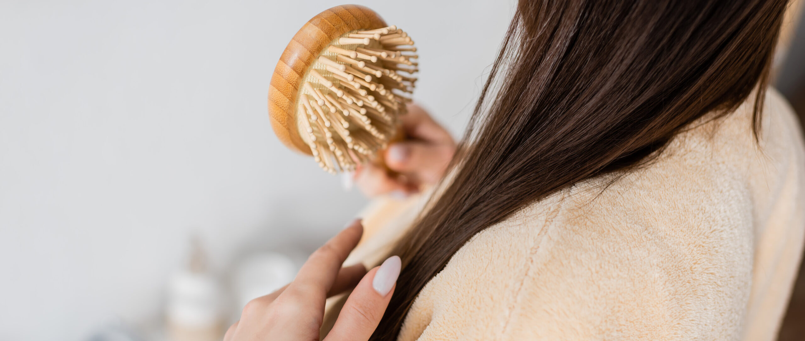 cropped view of young woman brushing shiny hair in bathroom